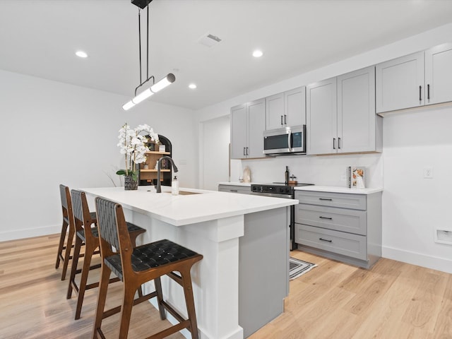 kitchen with appliances with stainless steel finishes, gray cabinetry, a sink, a breakfast bar, and an island with sink