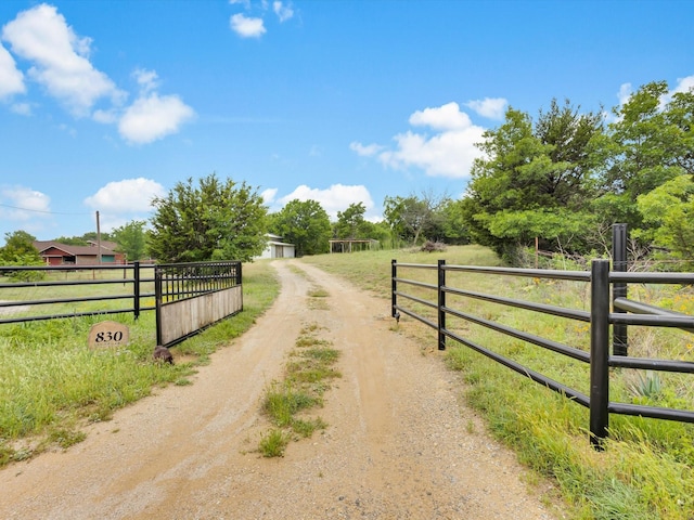 view of street with a gated entry, driveway, and a rural view