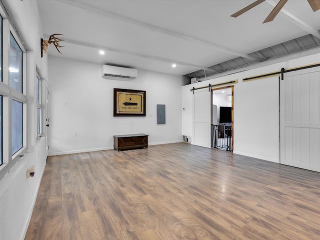 basement with a wall mounted air conditioner, ceiling fan, wood finished floors, and a barn door