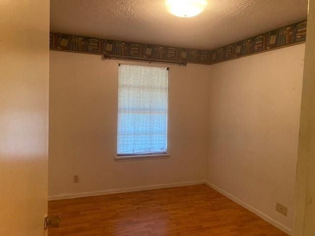 spare room with plenty of natural light, baseboards, a textured ceiling, and wood finished floors