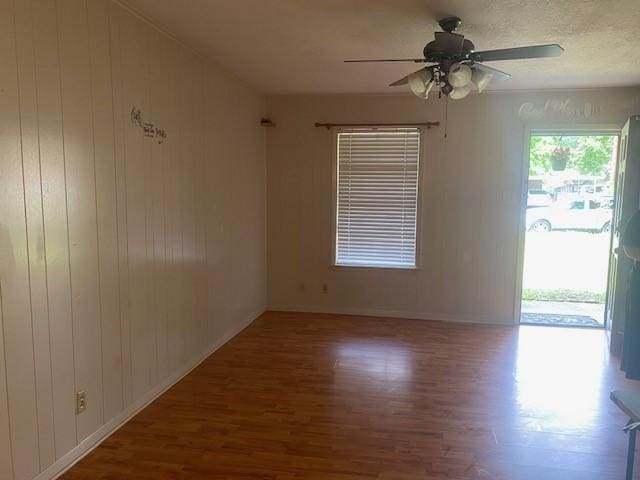 spare room with baseboards, a ceiling fan, wood finished floors, and wood walls