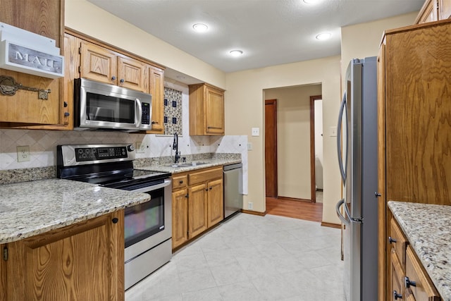 kitchen featuring light stone counters, a sink, appliances with stainless steel finishes, and backsplash