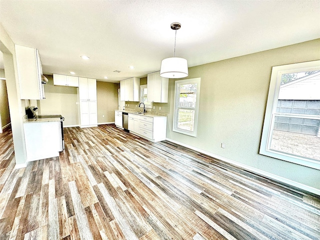 kitchen featuring stainless steel dishwasher, a sink, baseboards, light wood finished floors, and white cabinetry