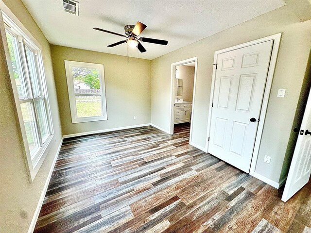 unfurnished bedroom featuring visible vents, wood finished floors, baseboards, ensuite bathroom, and a ceiling fan
