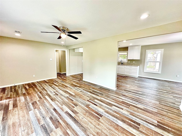 unfurnished living room featuring a sink, light wood-style floors, a ceiling fan, baseboards, and visible vents