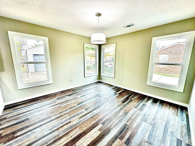 unfurnished dining area featuring baseboards, a textured ceiling, wood finished floors, and visible vents