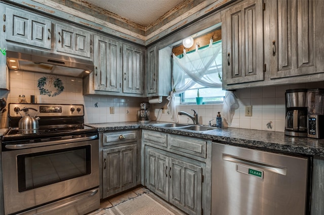 kitchen with stainless steel appliances, under cabinet range hood, a sink, dark countertops, and decorative backsplash