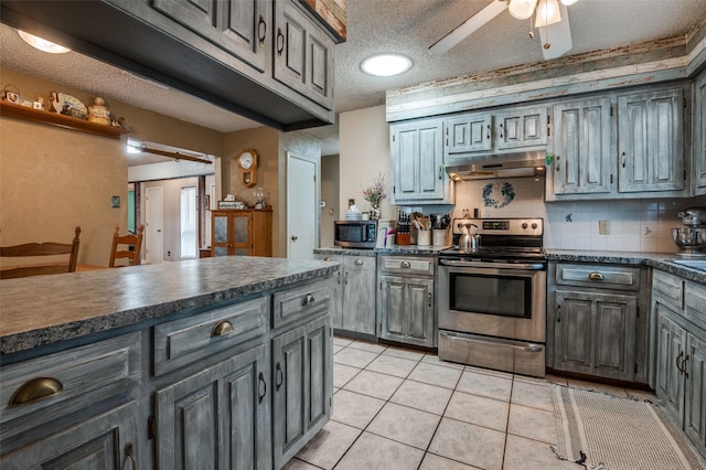 kitchen with gray cabinets, a textured ceiling, dark countertops, under cabinet range hood, and stainless steel appliances