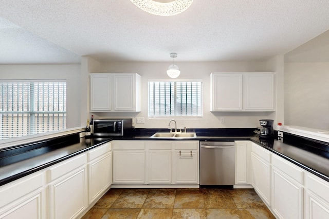 kitchen featuring a textured ceiling, appliances with stainless steel finishes, dark countertops, a sink, and white cabinetry
