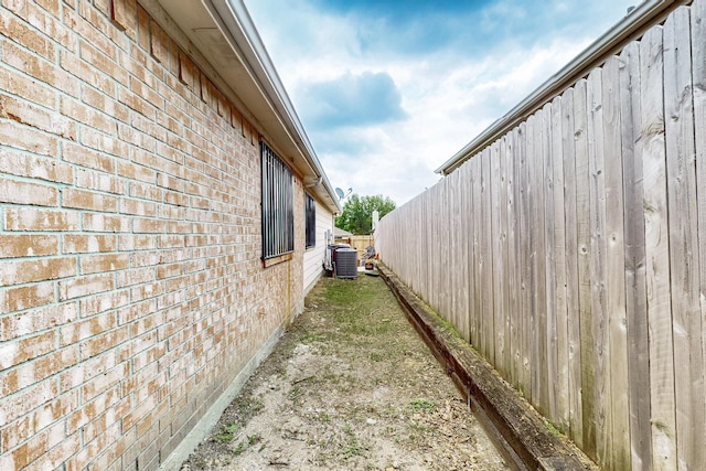 view of side of property with fence, cooling unit, and brick siding