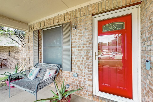 view of exterior entry with brick siding and a porch