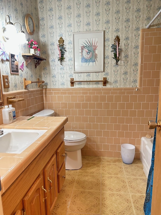 bathroom with tile patterned flooring, vanity, toilet, tile walls, and wallpapered walls