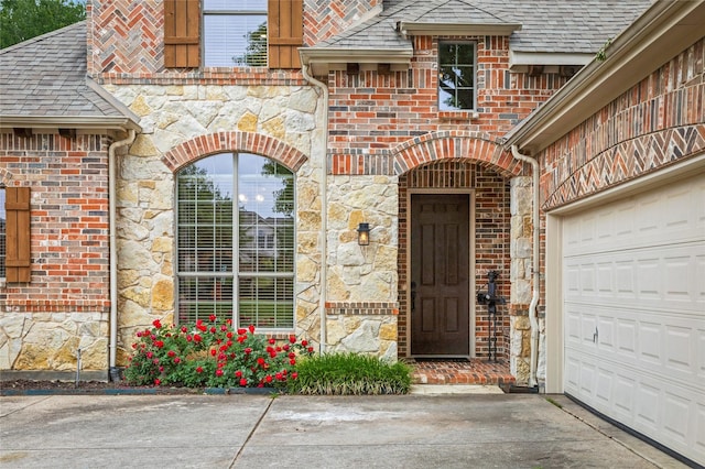 doorway to property featuring roof with shingles, stone siding, and concrete driveway