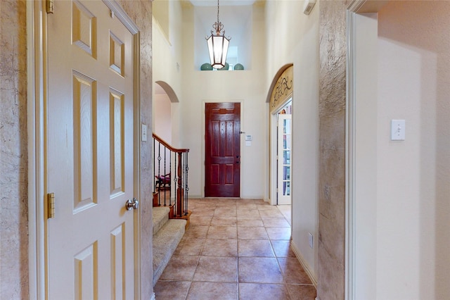 entrance foyer featuring baseboards, a notable chandelier, a high ceiling, stairs, and light tile patterned flooring