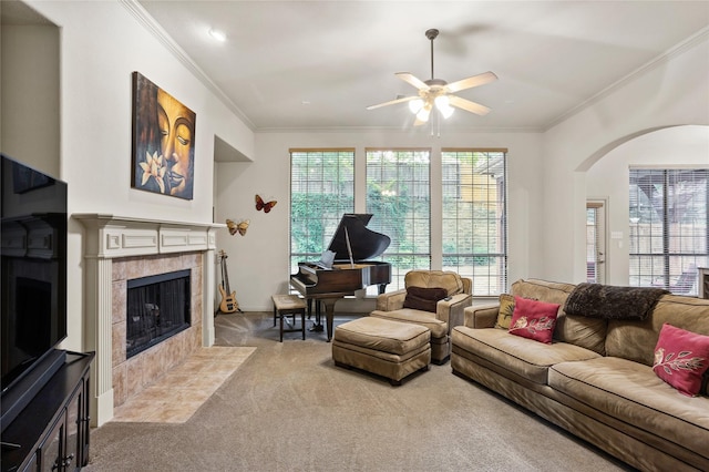 carpeted living room featuring crown molding, arched walkways, ceiling fan, and a tile fireplace