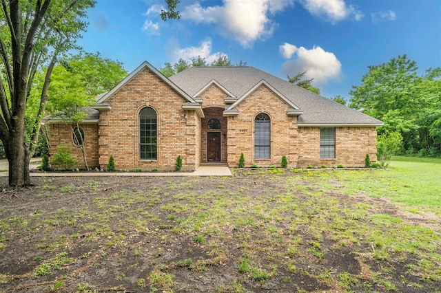 single story home with a shingled roof, a front yard, and brick siding