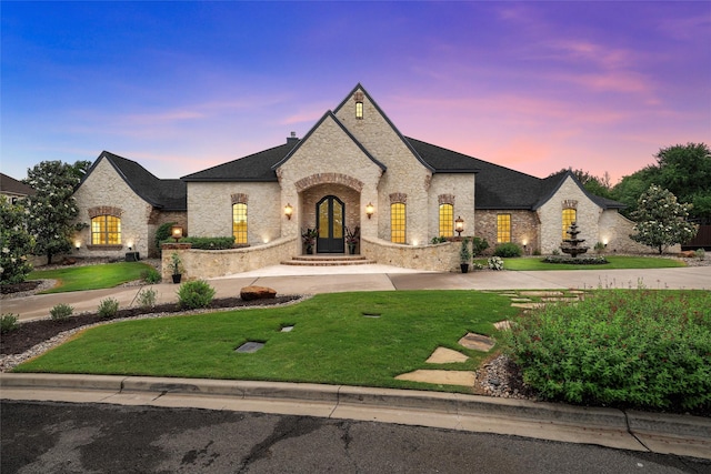 french country style house featuring a lawn, curved driveway, and brick siding