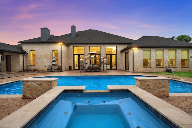 back of house at dusk featuring a patio, a pool with connected hot tub, and a chimney
