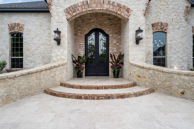 doorway to property with french doors, a shingled roof, and stone siding