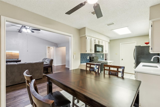 dining space with ceiling fan, a textured ceiling, wood finished floors, lofted ceiling, and visible vents