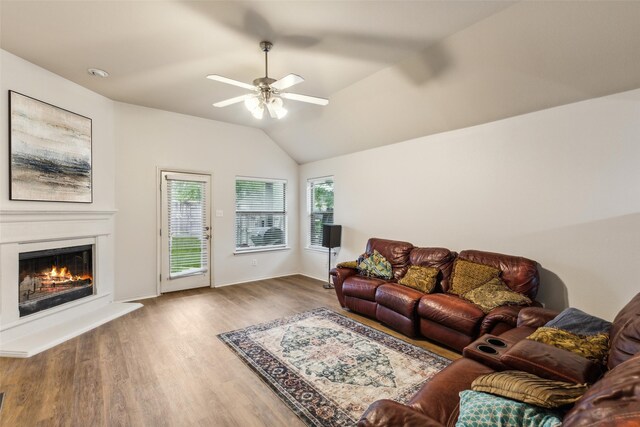 living area with wood finished floors, a ceiling fan, a lit fireplace, vaulted ceiling, and baseboards