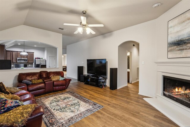 living area with lofted ceiling, wood finished floors, ceiling fan, arched walkways, and a glass covered fireplace