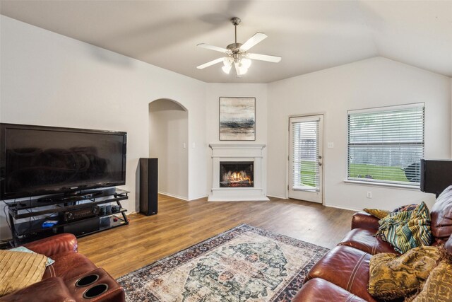 living room featuring arched walkways, wood finished floors, ceiling fan, a lit fireplace, and vaulted ceiling