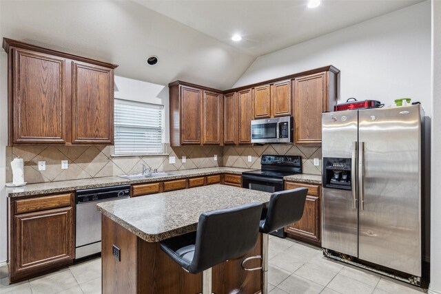 kitchen featuring appliances with stainless steel finishes, vaulted ceiling, a center island, decorative backsplash, and a sink