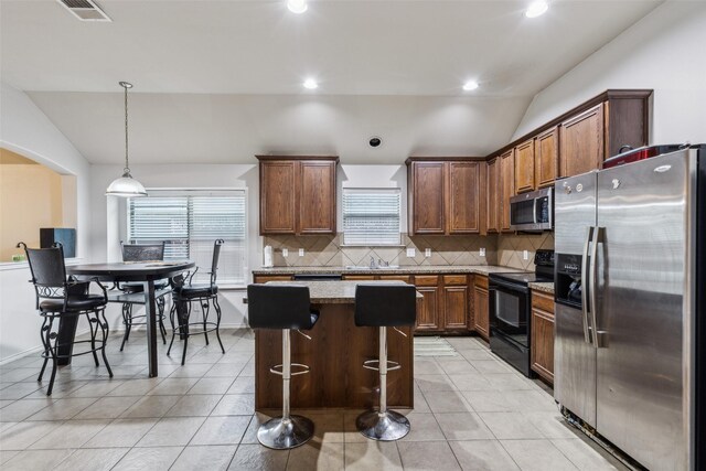 kitchen featuring appliances with stainless steel finishes, lofted ceiling, decorative backsplash, a kitchen island, and light tile patterned floors