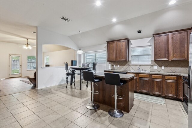 kitchen featuring decorative backsplash, a center island, light tile patterned floors, lofted ceiling, and pendant lighting