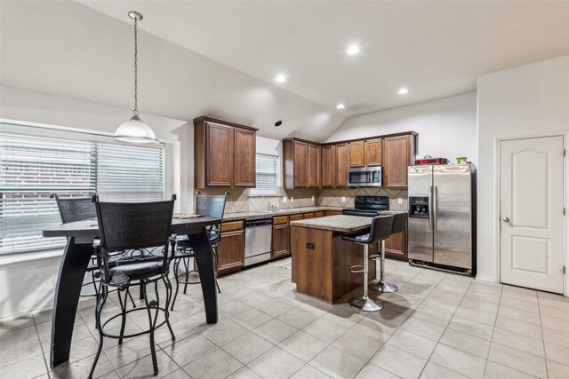 kitchen with appliances with stainless steel finishes, tasteful backsplash, lofted ceiling, a kitchen island, and a kitchen breakfast bar