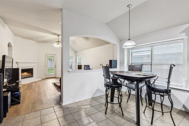 dining space featuring healthy amount of natural light, ceiling fan, vaulted ceiling, a warm lit fireplace, and tile patterned floors