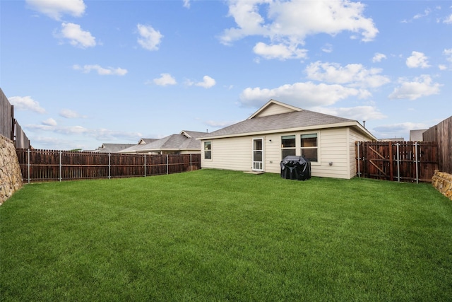 back of property with a lawn, a fenced backyard, and a shingled roof