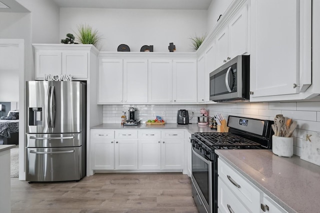 kitchen featuring light stone countertops, white cabinets, light wood finished floors, appliances with stainless steel finishes, and backsplash