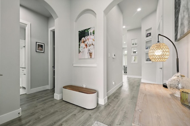 hallway featuring arched walkways, baseboards, recessed lighting, and wood finished floors
