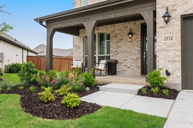 view of exterior entry with covered porch, brick siding, and fence