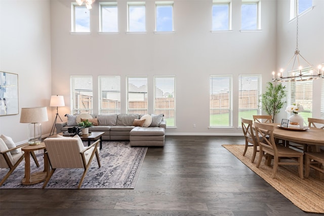 living room with baseboards, a towering ceiling, a notable chandelier, and dark wood-style floors