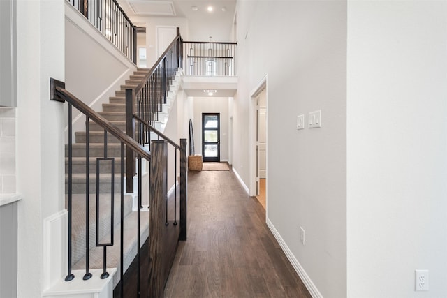 interior space featuring dark wood-type flooring, baseboards, a towering ceiling, and stairs