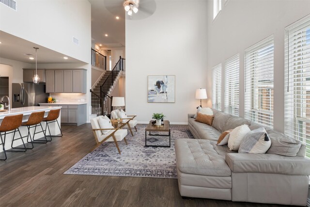 living area with visible vents, dark wood-style flooring, a towering ceiling, stairs, and ceiling fan
