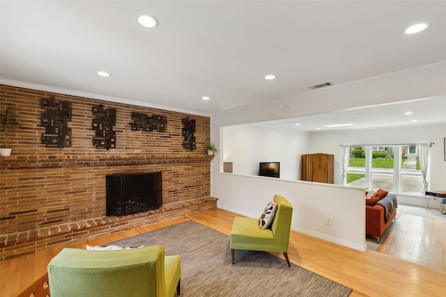 living room with a brick fireplace, recessed lighting, visible vents, and wood finished floors