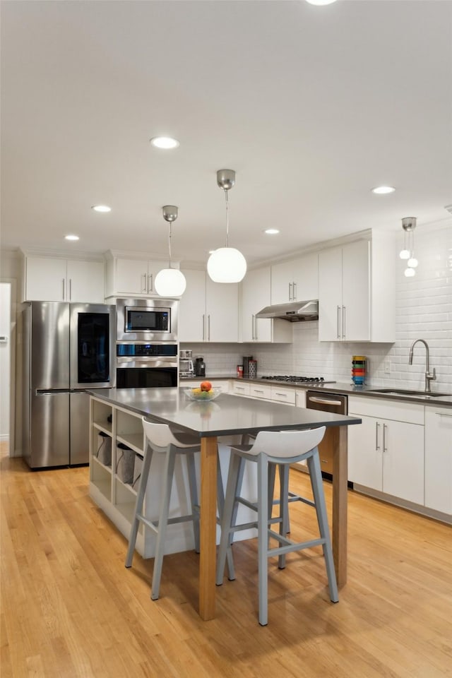 kitchen with backsplash, appliances with stainless steel finishes, dark countertops, a sink, and under cabinet range hood
