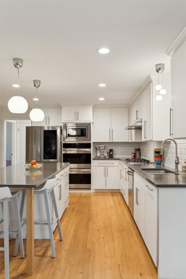kitchen featuring dark countertops, white cabinets, a sink, appliances with stainless steel finishes, and hanging light fixtures