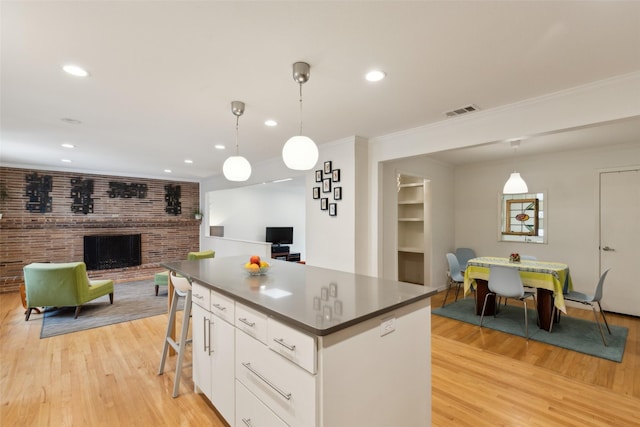 kitchen featuring visible vents, dark countertops, a brick fireplace, light wood finished floors, and open floor plan
