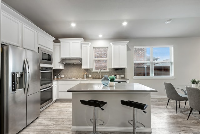 kitchen featuring a center island, stainless steel appliances, light wood-style flooring, and under cabinet range hood