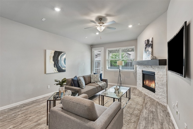 living area featuring baseboards, ceiling fan, a stone fireplace, and wood finished floors