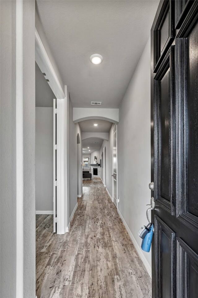 hall with arched walkways, baseboards, wood finished floors, and visible vents