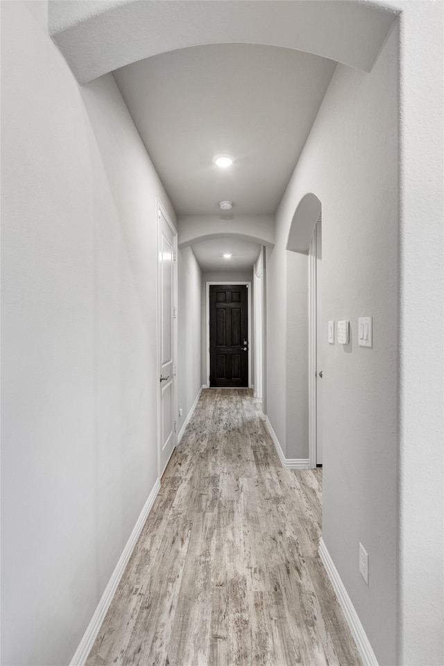 hallway featuring baseboards, arched walkways, and light wood finished floors