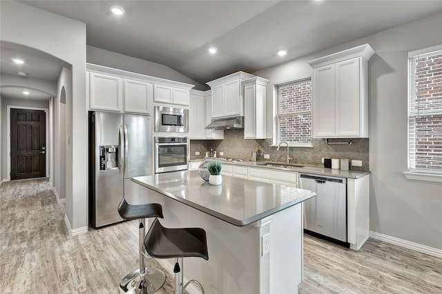 kitchen with light wood-type flooring, white cabinetry, under cabinet range hood, a sink, and stainless steel appliances