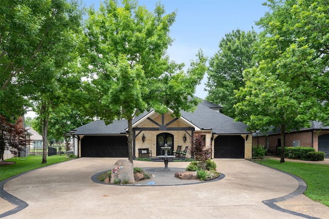 view of front of property featuring a front yard, stone siding, curved driveway, a shingled roof, and an attached garage