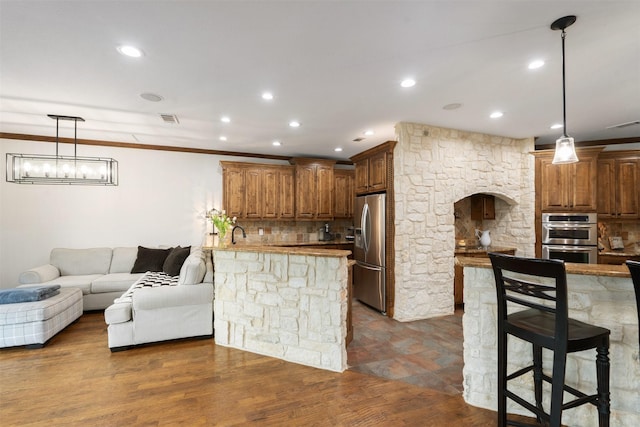 kitchen featuring stainless steel appliances, open floor plan, decorative light fixtures, a peninsula, and backsplash